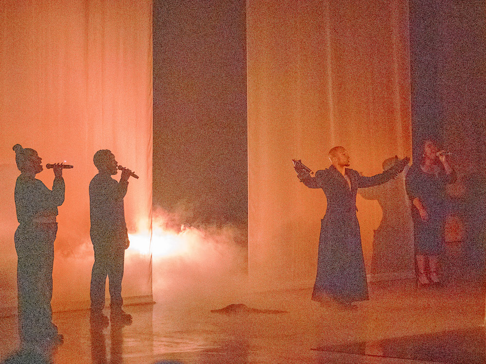 a group of performers on a stage lit in orange and yellow tones